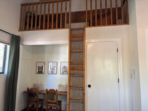 Een kamer met een hoogslaper, een houten trap, een bureau met stoelen, en ingelijste foto's aan de muur.