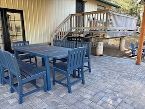 A patio with a table and chairs, a grill, and a wooden deck.