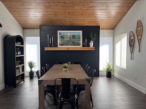 A dining area with a wooden table and chairs, a black bookshelf, and a framed landscape painting on the wall.