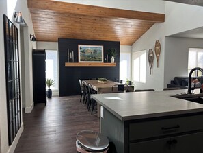 Een moderne keuken met een centraal eiland, houten plafond en een zithoek met stoelen.