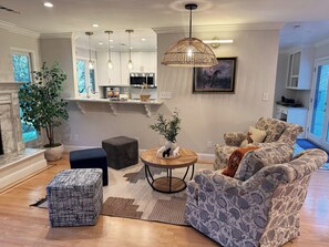 A modern living room with a sofa, ottoman, and coffee table, a kitchen with white cabinets and stainless steel appliances, and a large window with a view. - Lafayette Hills 3BR Private Family Getaway Near Walnut Creek (Lafayette)
