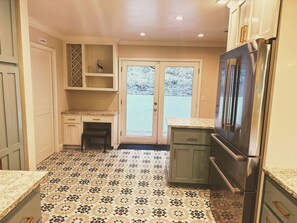 Une cuisine avec un carrelage décoratif, un réfrigérateur et une porte donnant sur l’extérieur.