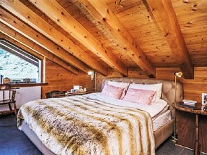 A wooden cabin bedroom with a large bed, a nightstand, and a window. - Antara in Grindelwald by Interhome (Grindelwald)
