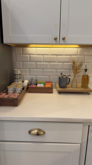 Een keuken met witte kasten, een houten aanrechtblad en diverse keukenspullen, waaronder een koffiezetapparaat, een vaas met korelscheuten en een fles.