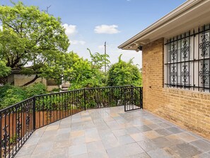 A paved outdoor area with a curved black metal railing, a brick building with decorative window bars, and lush green trees in the background. - Spacious Houston Retreat Sleeps 26 (Houston)