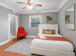 A bedroom with a bed, a red chair, a ceiling fan, a window with blinds, and artwork on the walls. - Spacious Houston Retreat Sleeps 26 (Houston)