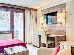 Une chambre d’hôtel avec un lit, un bureau et une chaise. Il y a une fenêtre avec des rideaux, un radiateur et une lampe fixée au mur.