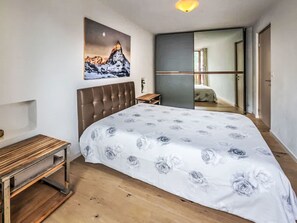 Une chambre à coucher avec un lit, une table de chevet, un banc en bois, un tableau au mur et une vue sur une autre pièce.
