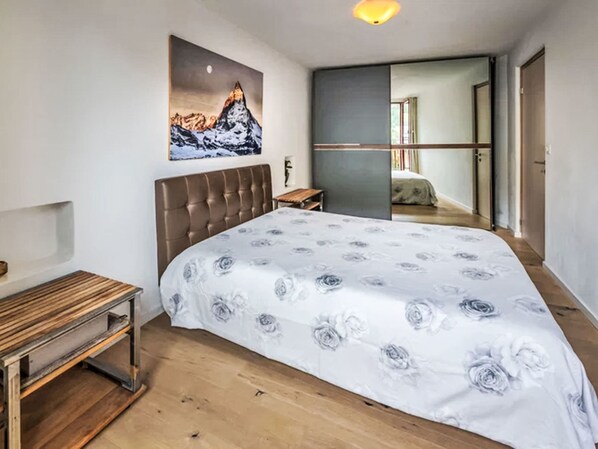 Een slaapkamer met een bed, een nachtkastje, een houten bankje, een schilderij aan de muur en uitzicht op een andere kamer.