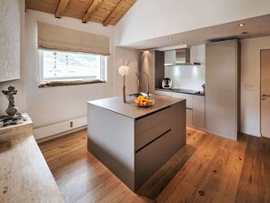 A modern kitchen with a central island, wooden flooring, and a window with a view. - 4BR Clémenceau Duplex Penthouse by Interhome (Verbier)