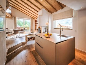 Une cuisine moderne dotée d’un îlot central, de planchers en bois et offrant une vue sur l’extérieur.