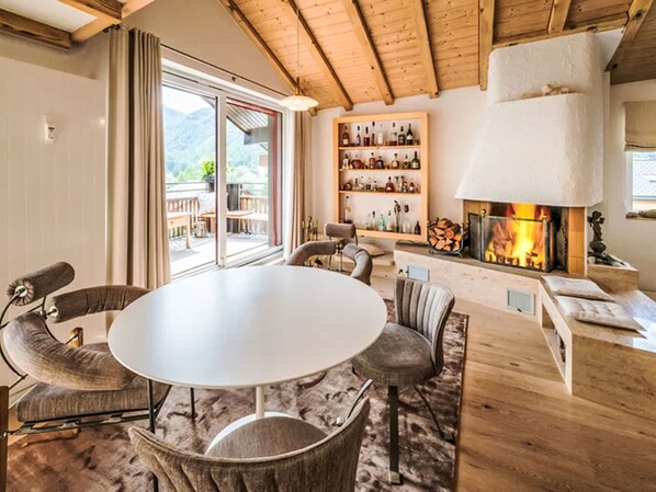 Un salon chaleureux avec une table ronde, des sièges confortables, une cheminée et une bibliothèque remplie de divers objets.