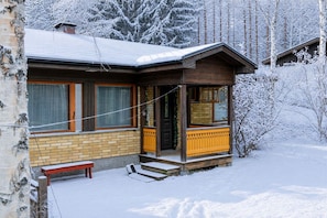 Une cabane en bois avec des fondations en briques, une véranda dotée d’une balustrade en bois et un banc.