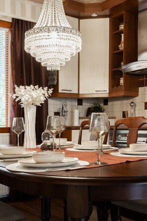 Un coin repas agrémenté d’un lustre, d’un centre de table composé de fleurs blanches et d’une table dressée avec des assiettes, des verres et des couverts.