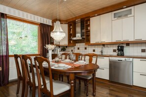 A dining area with a wooden table set for four, surrounded by chairs. A chandelier hangs above the table. - Ounasrinne 3BR House, Sauna By Lapland Host (Rovaniemi)