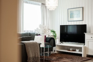 Een moderne woonkamer met een bank, een glazen salontafel, een tv op een standaard en een decoratieve plant.