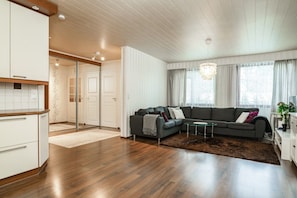 A modern living room with a sectional sofa, a glass coffee table, and a chandelier. - Ounasrinne 3BR House, Sauna By Lapland Host (Rovaniemi)