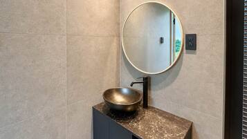 Une salle de bain avec un miroir rond, un lavabo sur colonne et un porte-serviettes.