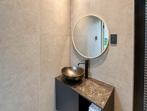 Une salle de bain avec un miroir rond, un lavabo sur colonne et un porte-serviettes.