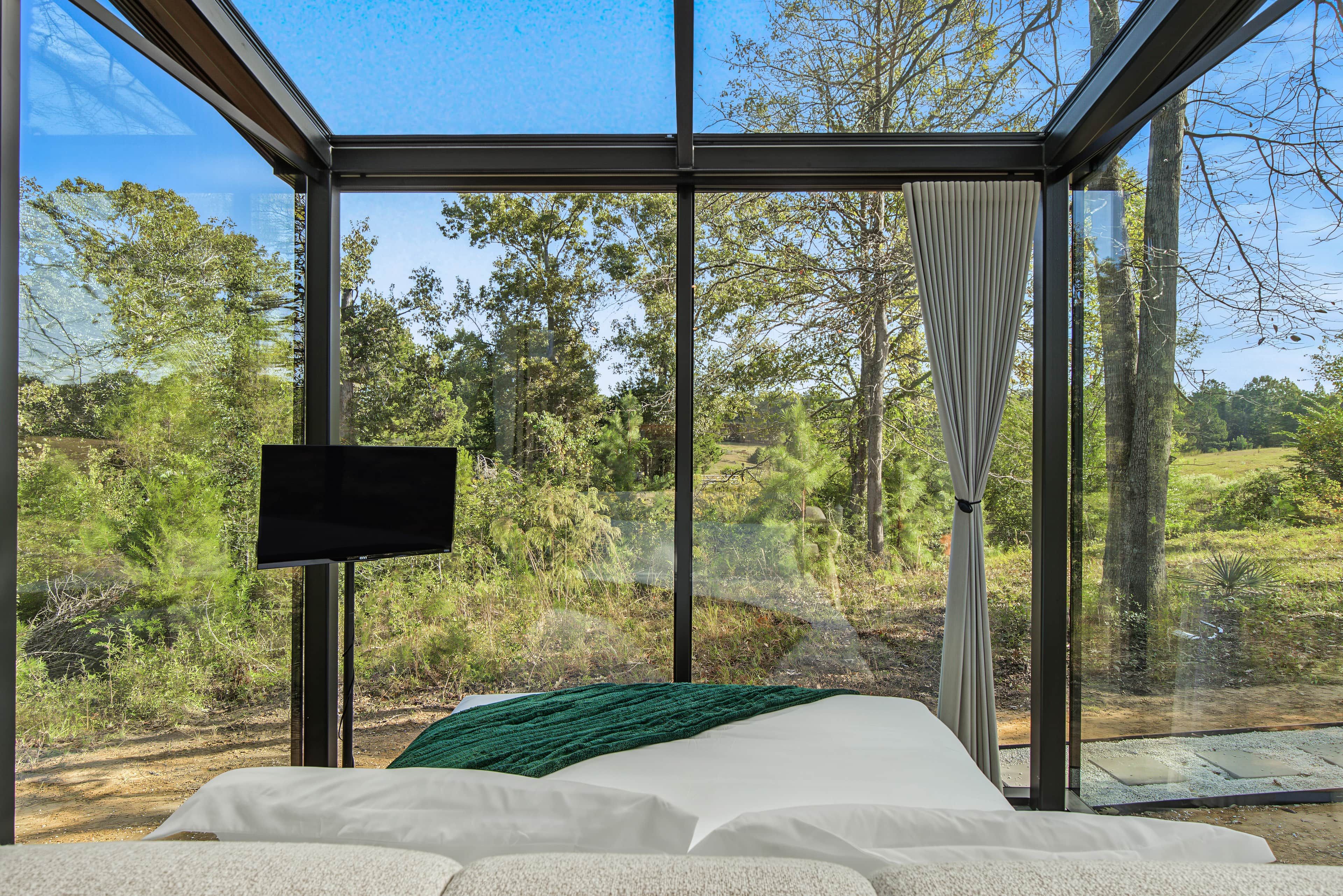 Ein Schlafzimmer mit großem Fenster, einem Bett und einem Flachbildfernseher.