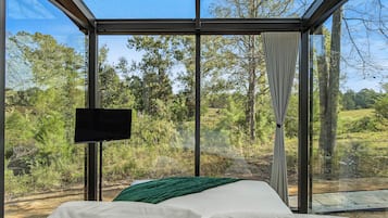 A bedroom with a large window, a bed, and a flat-screen TV.