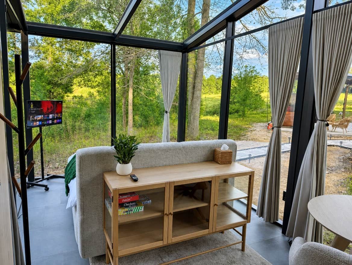 A modern room with a glass enclosure, a sofa, a wooden console table, and a view of greenery outside.