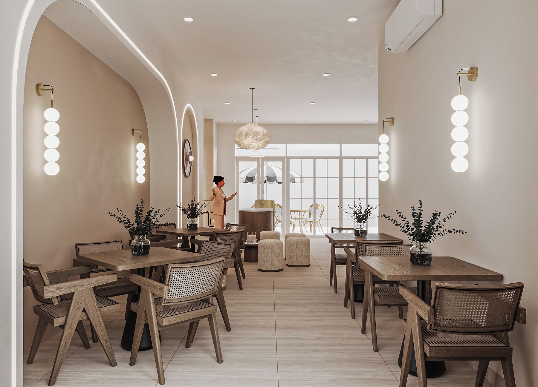 Un comedor moderno con mesas y sillas de madera, una mujer de pie e iluminación colgante.