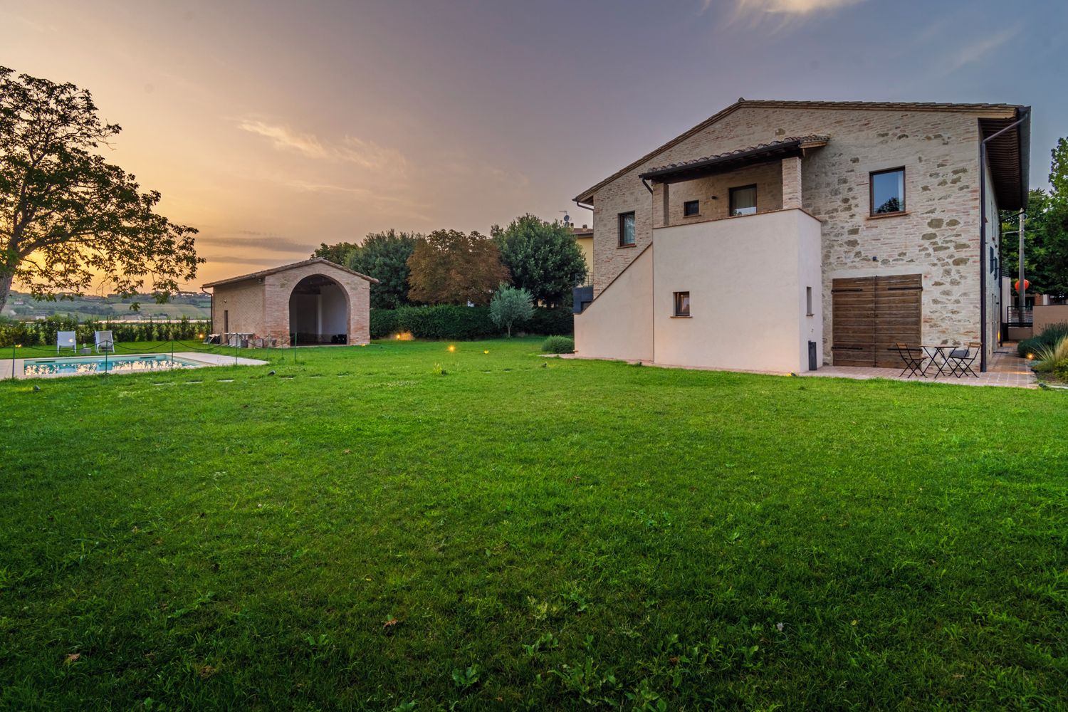 A modern house with a stone facade, a large lawn, and a swimming pool.