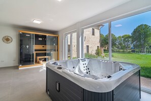 Un baño moderno con una bañera grande, cabina de ducha con mampara de vidrio y vistas a un edificio de ladrillo y vegetación.