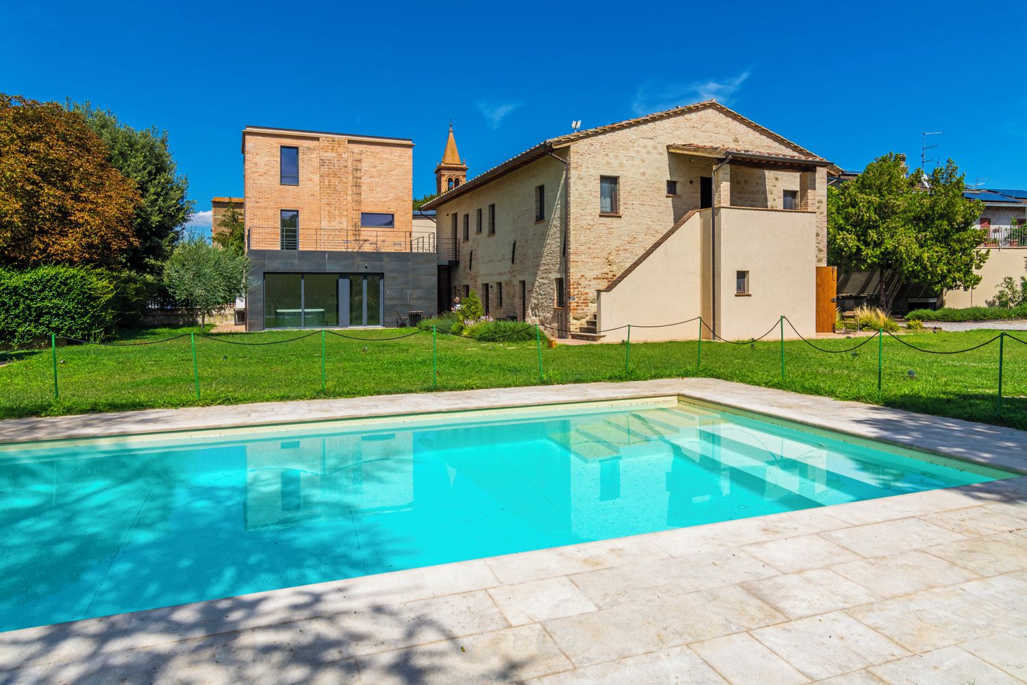A swimming pool with a clear blue water surface, surrounded by a paved area and a grassy lawn.