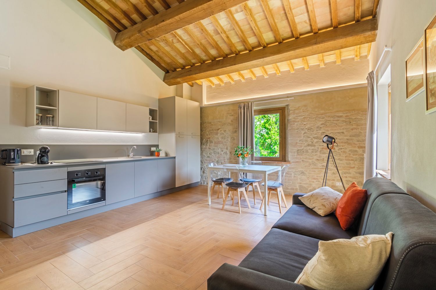 A modern kitchen with built-in appliances, a dining area with a table and chairs, and a cozy seating area with a sofa and cushions.