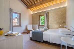 Un dormitorio con cama, una silla, una mesita de noche y una ventana.