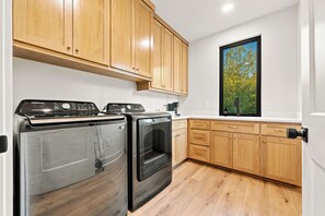 A kitchen with wooden cabinets, a stainless steel range, a dishwasher, and a window with a view of trees. - Luxe | Pool, Sauna, & Karaoke | Sleeps 16 (Garland County)