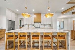 A modern kitchen with a large marble island, wooden chairs, and pendant lighting. - Luxe | Pool, Sauna, & Karaoke | Sleeps 16 (Garland County)