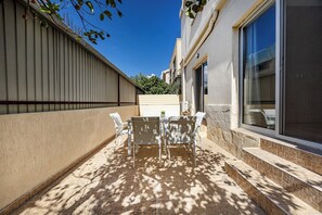 Une terrasse avec une table et des chaises, une fenêtre et un mur orné d’une plante.
