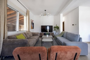 Sala de estar moderna com sofá, poltrona, TV e uma planta.