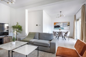 A modern living room with a grey sofa, a coffee table, and a dining area with chairs. - Gordonos – Modern 3Bed Apartment with Large Garden (Limassol)