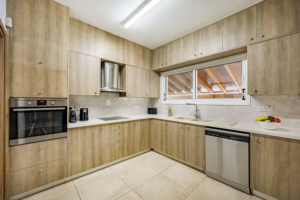 Une cuisine moderne avec des meubles en bois, un four encastré, un lave-vaisselle et une fenêtre donnant sur la structure du toit.