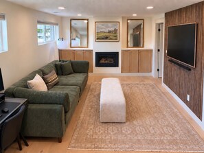 A modern living room with a green sofa, a flat-screen TV, a fireplace, and a large mirror. - Newly Renovated Riverwoods Retreat — 4BR, 3BA (Orem)
