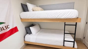Ein Stockbett mit Holzrahmen und weißer Bettwäsche, ein kleiner Teppich auf dem Boden und eine an der Wand befestigte Flagge.