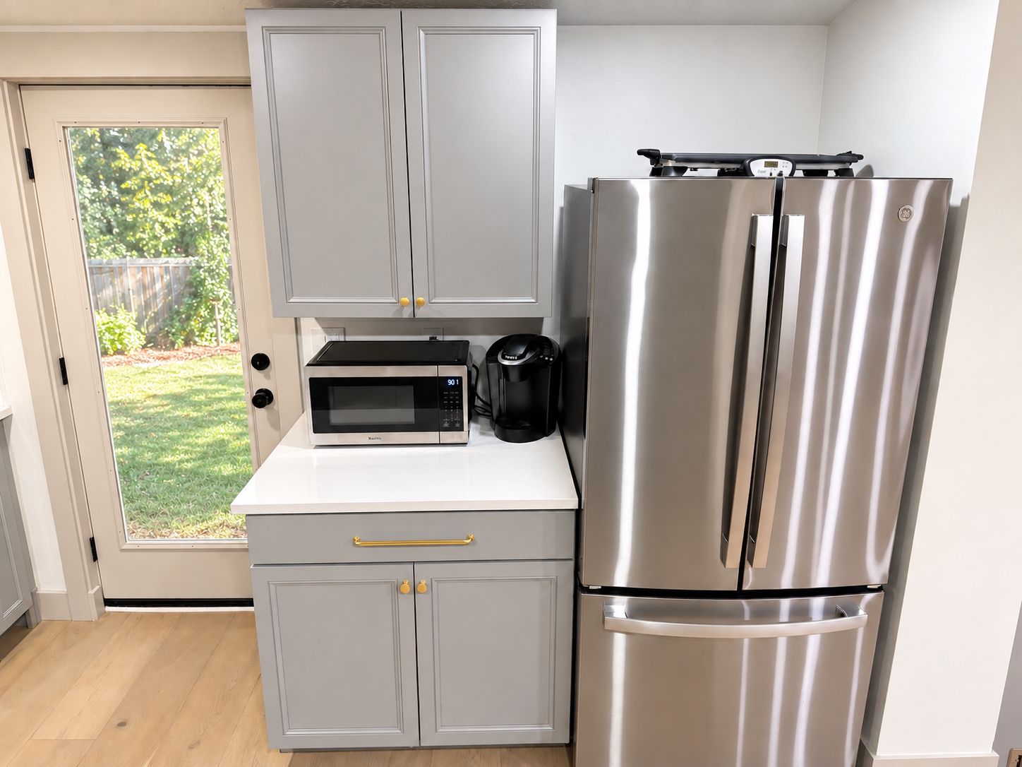 Eine kleine Küche mit Edelstahlkühlschrank, Mikrowelle und Kaffeemaschine auf einer weißen Arbeitsplatte.