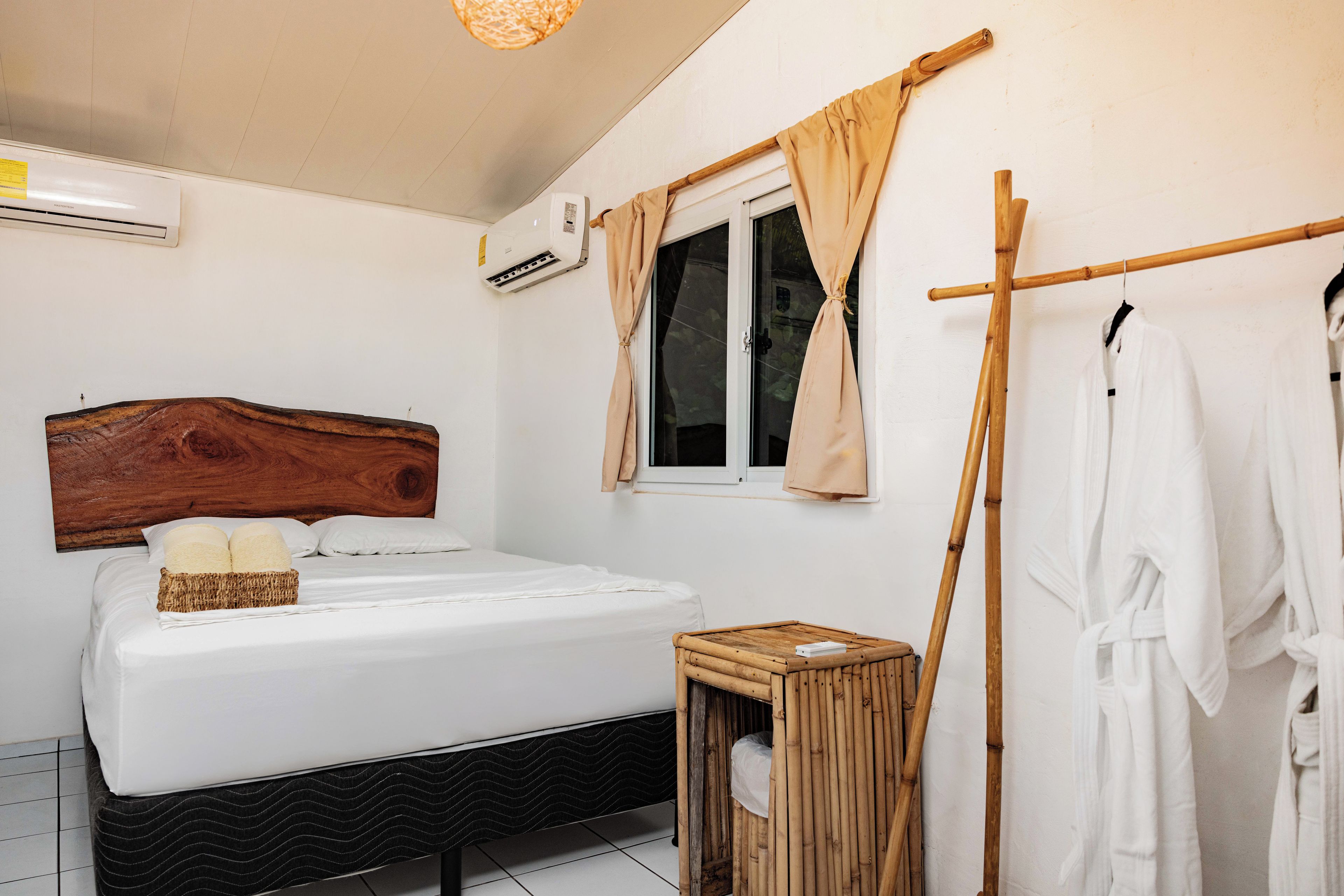 Une chambre à coucher avec une tête de lit en bois, un lit, une table de chevet, une fenêtre avec des rideaux et un climatiseur fixé au mur.
