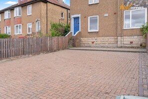 A paved courtyard with a wooden fence, a blue door, and a brick building with windows. - 3 bed by A720 City Bypass, sleeps 5, free parking (Edinburgh)