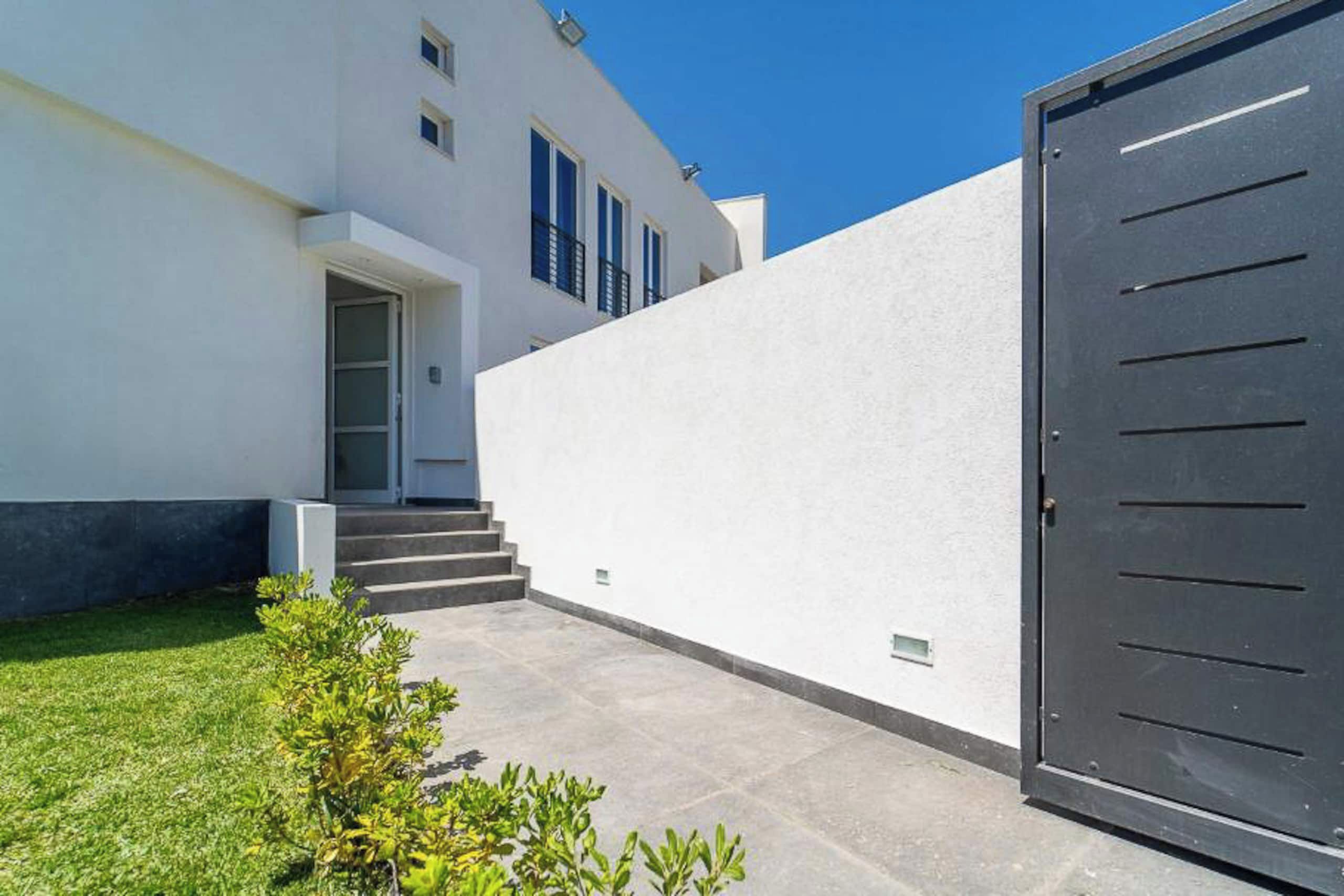 Un edificio moderno con fachada blanca, una puerta oscura y unos pocos escalones que llevan a una puerta.
