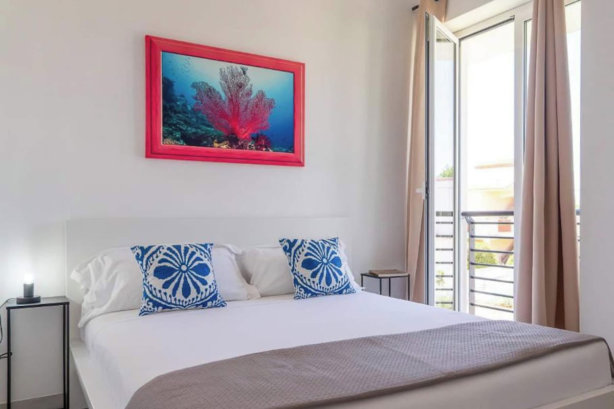 A hotel room with a bed, two pillows, a nightstand, a lamp, and a framed picture on the wall.