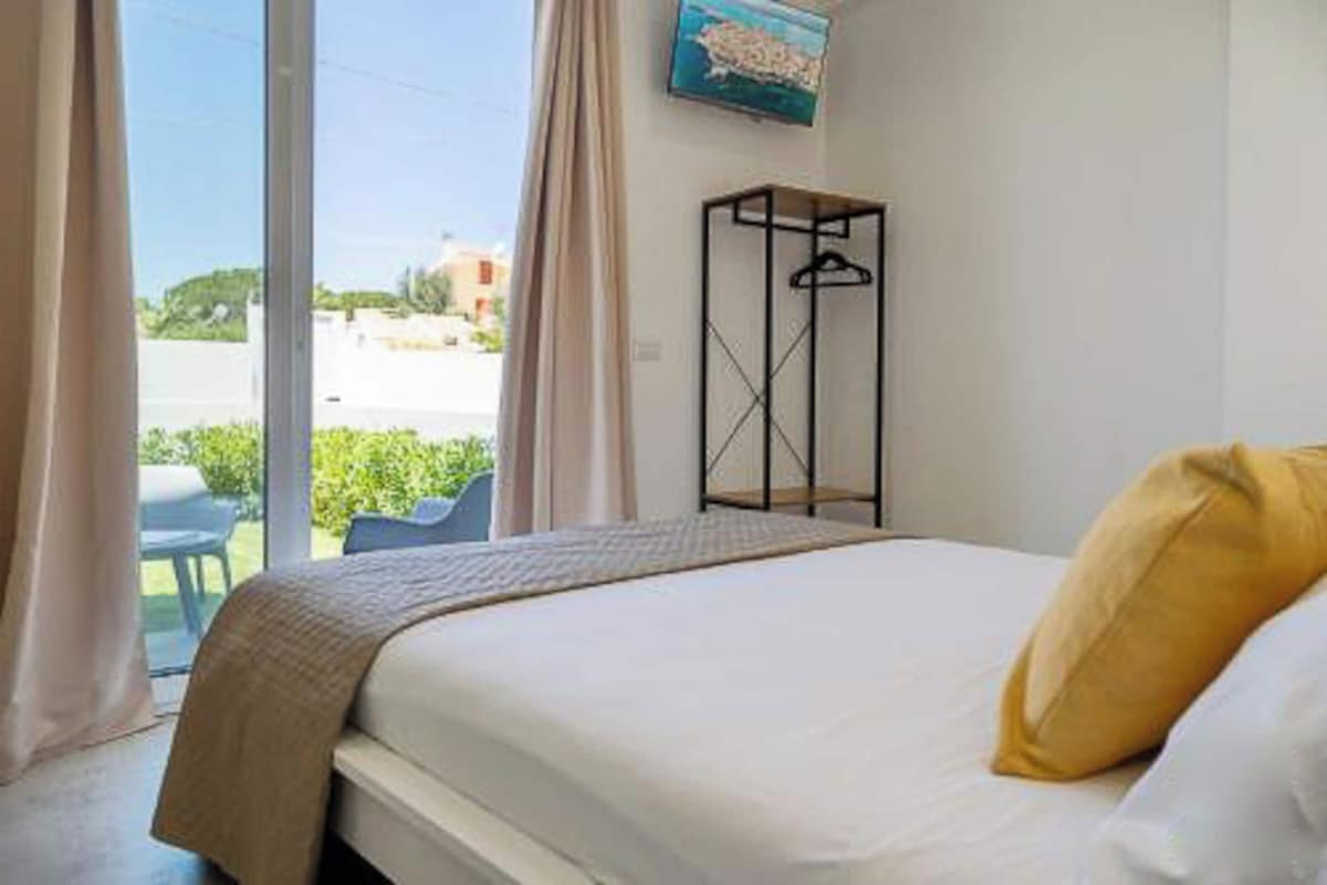 A hotel room with a bed, a hanging coat rack, and a view of the outside.