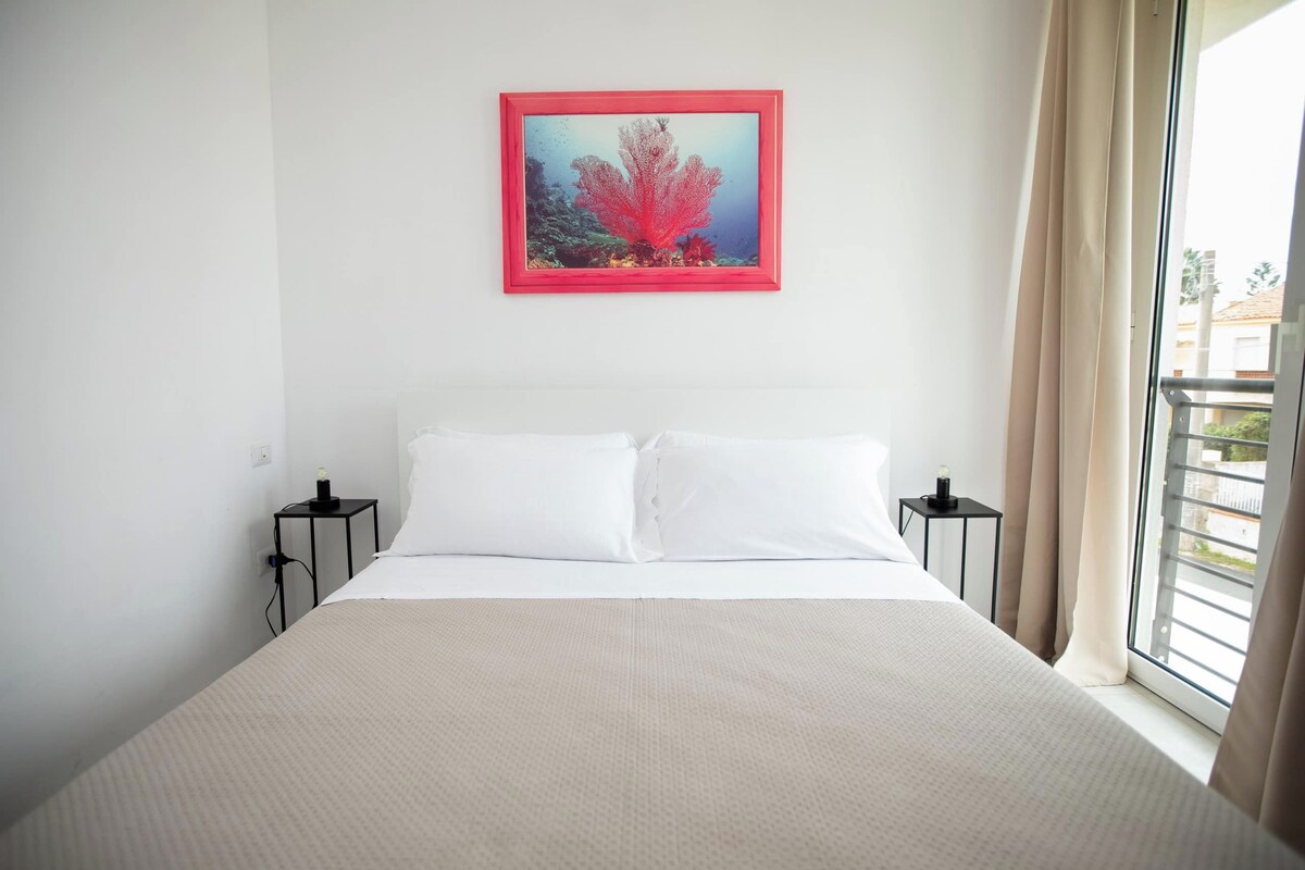 A hotel room with a bed, two bedside tables, a window with curtains, and a framed picture on the wall.