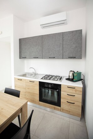 A modern kitchen with grey cabinets, a gas stove, a built-in oven, and a coffee machine. - Golden Bay Apartments (Arenella)