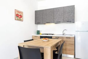 A modern kitchen with grey cabinets, a wooden table, and a bowl of fruit. - Golden Bay Apartments (Arenella)