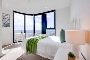 A modern bedroom with a large bed, a desk, and a view of the city through large windows. - StayAU High-Rise Luxury in CBD Apt @EQ Tower (Melbourne)